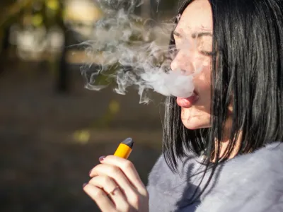 The girl smokes an electronic cigarette on the street.