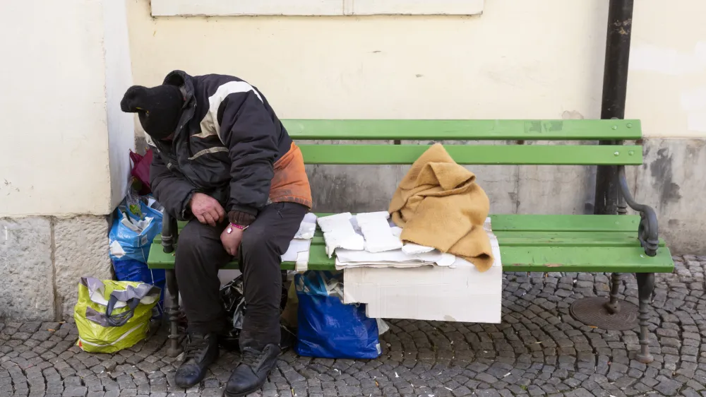 Homeless man in dirty clothes sleeps on a green bench in the center of Ljubljana, Slovenia.