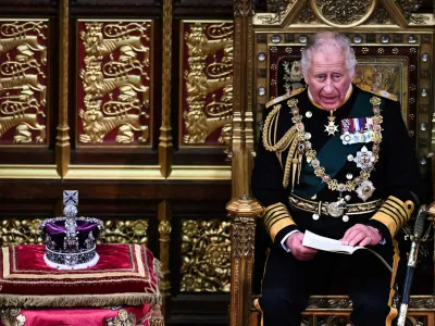 Britain's Prince Charles reads the Queen's speech as he sits by the The Imperial State Crown in the House of Lords Chamber, flanked by Britain's Prince William, left, and Camilla, Duchess of Cornwall, during the State Opening of Parliament, in the Houses of Parliament, in London, Tuesday, May 10, 2022. Britain's Conservative government made sweeping promises to cut crime, improve health care and revive the pandemic-scarred economy as it laid the laws it plans in the next year in a tradition-steeped ceremony known as the Queen's Speech -- but without a key player, Queen Elizabeth II, absent for the first time in six decades. The 96-year-old monarch pulled out of the ceremonial State Opening of Parliament because of what Buckingham Palace calls "episodic mobility issues." Her son and heir, Prince Charles, stood in, rattling through a short speech laying out 38 bills the government plans to pass. (Ben Stansall/Pool Photo via AP)