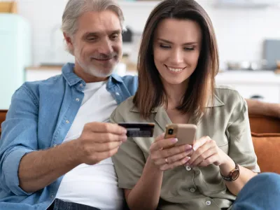 Smiling caucasian couple involved in online shopping, entering payment information from credit bank card in mobile application, satisfied with quick money transfer, modern tech concept.