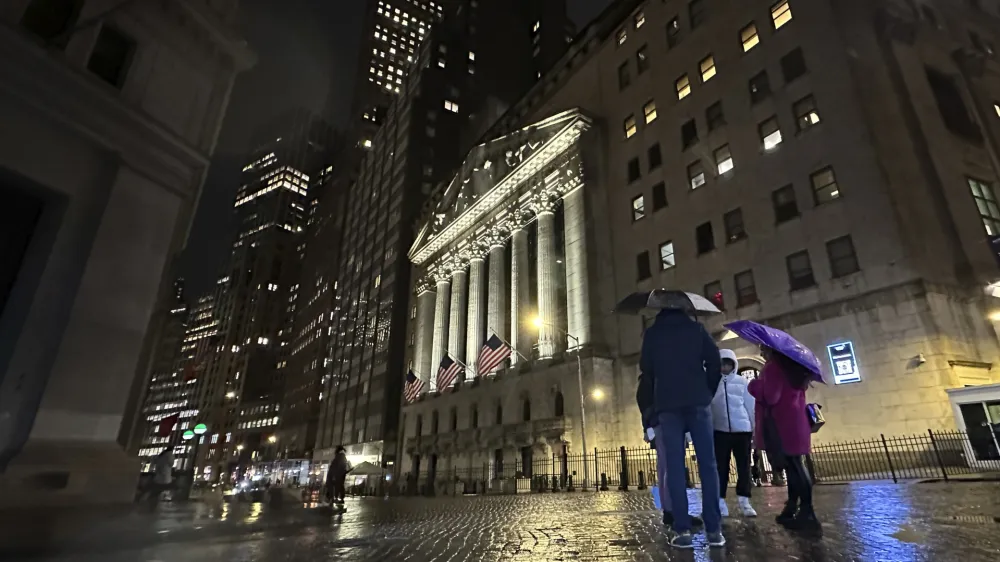 File - People huddle outside the New York Stock Exchange on Tuesday, Nov. 21, 2023 in New York. (AP Photo/Peter Morgan, File)