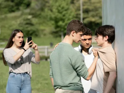 Two bullies menacing teenager boy and girl filming on phone. Cyber bullying and violence concept.