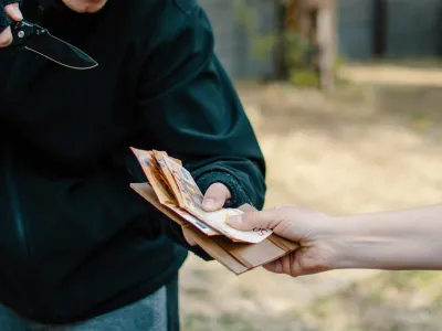 Unrecognizable Thief taking on force the money from the female hand outdoor. Man with knife Stealing Euro banknote paper currency cash from a woman on the street. Closeup robbery and criminal concept