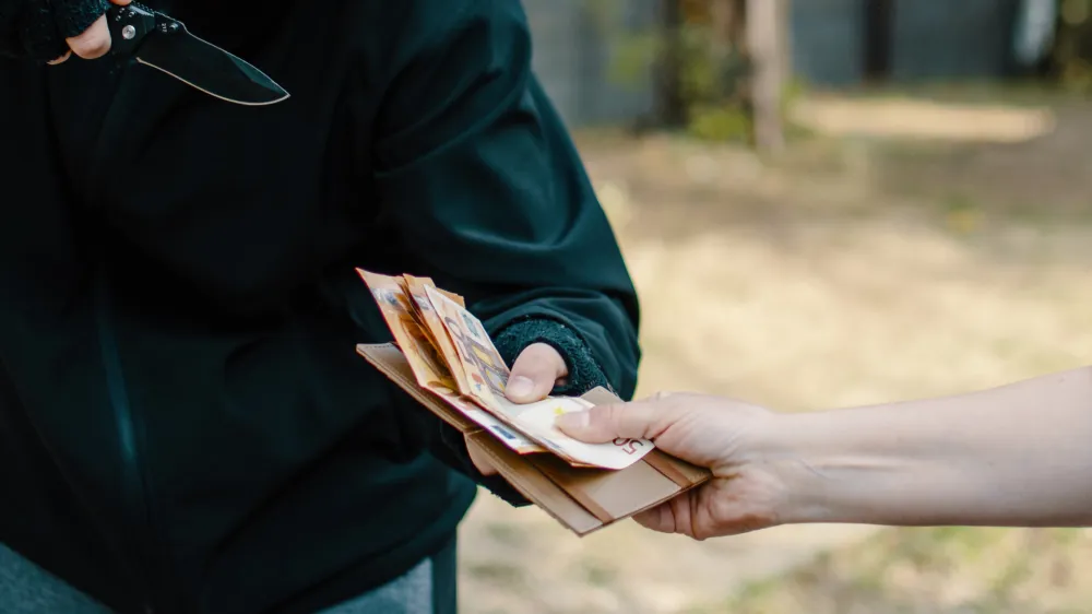 Unrecognizable Thief taking on force the money from the female hand outdoor. Man with knife Stealing Euro banknote paper currency cash from a woman on the street. Closeup robbery and criminal concept