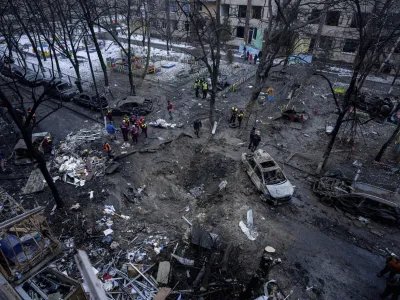 People stand near a crater in the yard of a damaged multi-store building after a Russian attack at residential neighbourhood in Kyiv, Ukraine, Wednesday, Dec. 13, 2023. (AP Photo/Evgeniy Maloletka)