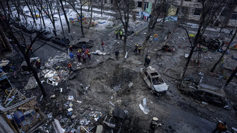 People stand near a crater in the yard of a damaged multi-store building after a Russian attack at residential neighbourhood in Kyiv, Ukraine, Wednesday, Dec. 13, 2023. (AP Photo/Evgeniy Maloletka)