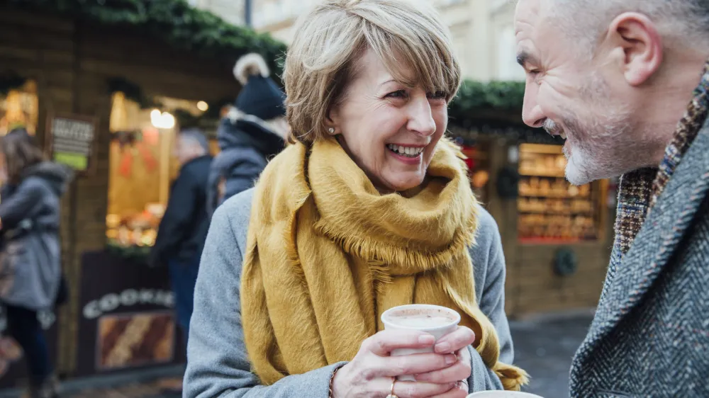 Mature couple are enjoying a cup of coffee as they explore the town christmas market.