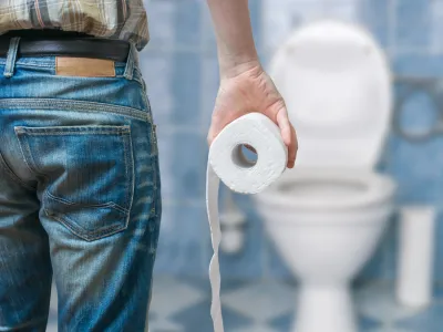 ﻿Man suffers from diarrhea holds toilet paper roll in front of toilet bowl.