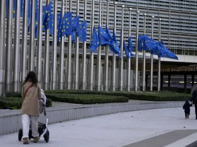 Pedestrians walk past as European Union flags flap in the wind at half staff, in remembrance of former European Commission President Jacques Delors, in front of European Union headquarters in Brussels, Thursday, Dec. 28, 2023. Delors, a Paris bank messenger's son who became the visionary and builder of a more unified Europe in his momentous decade as chief executive of the European Union, has died in Paris, his daughter Martine Aubry said Wednesday Dec. 27, 2023. He was 98. (AP Photo/Virginia Mayo)