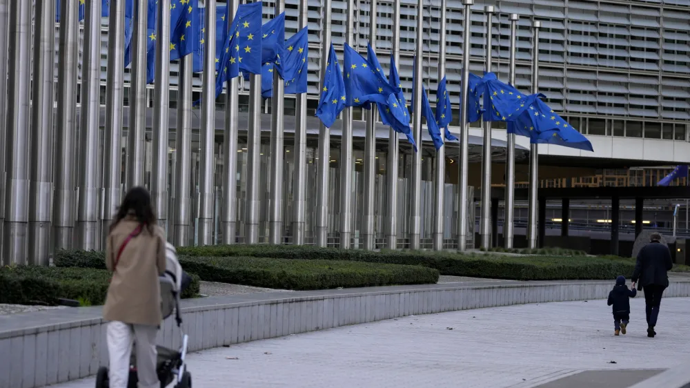 Pedestrians walk past as European Union flags flap in the wind at half staff, in remembrance of former European Commission President Jacques Delors, in front of European Union headquarters in Brussels, Thursday, Dec. 28, 2023. Delors, a Paris bank messenger's son who became the visionary and builder of a more unified Europe in his momentous decade as chief executive of the European Union, has died in Paris, his daughter Martine Aubry said Wednesday Dec. 27, 2023. He was 98. (AP Photo/Virginia Mayo)