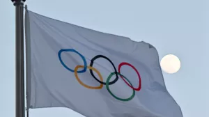 FILED - 14 February 2022, China, Beijing: The moon can be seen behind the flag with the Olympic rings. Photo: Peter Kneffel/dpa