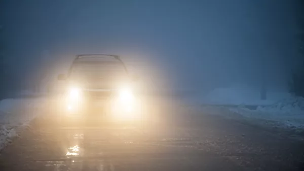 ﻿Bright headlights of a car driving on foggy winter road