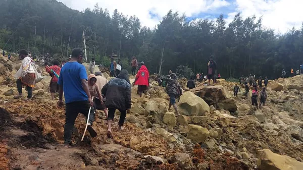 In this photo provides the International Organization for Migration, people cross over the landslide area to get to the other side in Yambali village, Papua New Guinea, Friday, May 24, 2024. More than 100 people are believed to have been killed in the landslide that buried a village and an emergency response is underway, officials in the South Pacific island nation said. The landslide struck Enga province, about 600 kilometers (370 miles) northwest of the capital, Port Moresby, at roughly 3 a.m., Australian Broadcasting Corp. reported. (Benjamin Sipa/International Organization for Migration via AP)