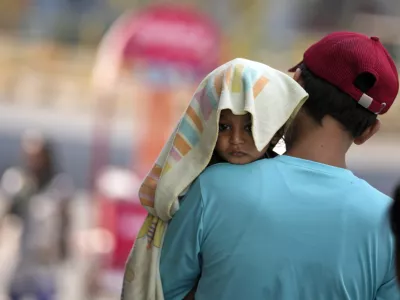 A man carries a child with its head covered with a towel to protect it from the heat in Jammu, India, Sunday, June 2, 2024. (AP Photo/Channi Anand)