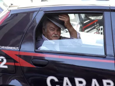 An unidentified man doffs his hat, as he rides in a Carabinieri (Paramilitary police) car after being arrested in Reggio Calabria, southern Italy, Tuesday, July 13, 2010, following one of the biggest operations ever against the powerful 'ndrangheta crime organization, in which 300 people were arrested including top bosses, and million of dollars (euros) in property seized. The pre-dawn raids Tuesday involved some 3,000 police across the country. Charges include murder, extortion, arms and drug trafficking and criminal association. Investigators described the operation as one of biggest blows ever to an organization that today is considered more powerful than the Sicilian Mafia. (AP Photo/Adriana Sapone)