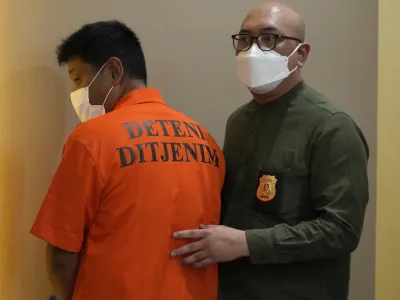 Immigration officers escort Mitsuhiro Taniguchi, 47, of Japan, left, during a press conference at immigration office in Jakarta, Indonesia Wednesday, June 8, 2022. Authorities on the southern tip of Indonesia's Sumatra island arrested a Japanese fugitive accused of fraud in Japan in connection with the receipt of a massive amount of COVID-19 subsidies for small businesses in distress, police said Wednesday.(AP Photo/Achmad Ibrahim)