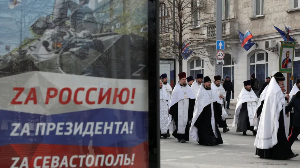 Clergymen walk past a board, displaying slogans with symbols "Z" in support of the Russian armed forces involved in the country's military campaign in Ukraine, during a religious procession to celebrate Orthodox Christmas in Sevastopol, Crimea, January 7, 2023. Slogans on a board read: "To Russia! To President! To Sevastopol!" REUTERS/Alexey Pavlishak