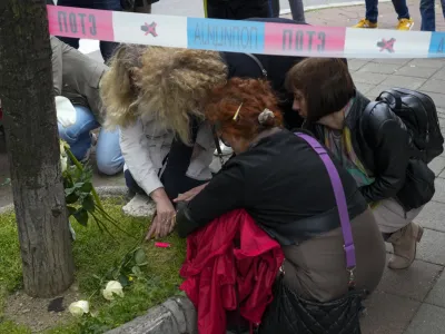 Women lay flowers and light candles for victims near the Vladislav Ribnikar school in Belgrade, Serbia, Wednesday, May 3, 2023. A 13-year-old who opened fire Wednesday at his school in Serbia's capital drew sketches of classrooms and wrote a list of people he intended to target in a meticulously planned attack, police said. (AP Photo/Darko Vojinovic)