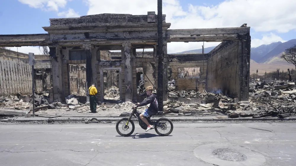 A boy rides along Main Street past wildfire damage on Friday, Aug. 11, 2023, in Lahaina, Hawaii. (AP Photo/Rick Bowmer)