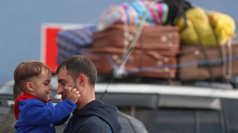 A refugee from Nagorno-Karabakh region holds a child while standing next to a car upon their arrival in the border village of Kornidzor, Armenia, September 26, 2023. REUTERS/Irakli Gedenidze   TPX IMAGES OF THE DAY