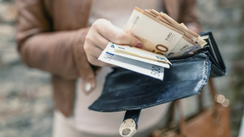 Woman holding in hands wallet with euro money. City girl is taking out money from wallet