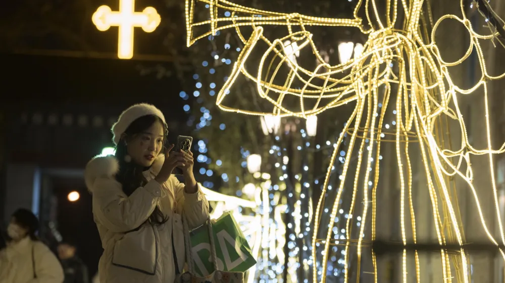 A visitor takes photos near light decorations outside Xishiku Church on Christmas Day in Beijing, Monday, Dec. 25, 2023. (AP Photo/Ng Han Guan)