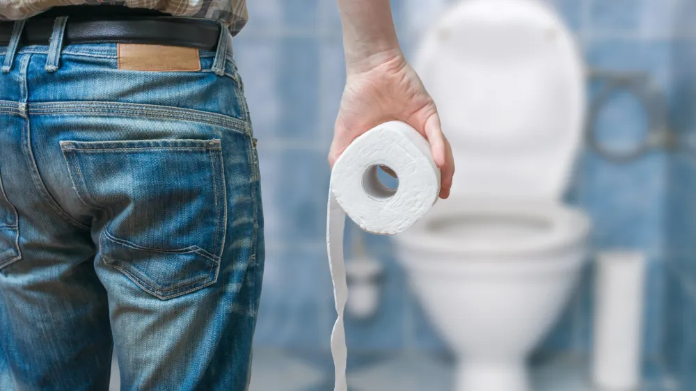 ﻿Man suffers from diarrhea holds toilet paper roll in front of toilet bowl.