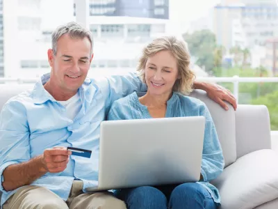 Smiling couple sitting on their couch using the laptop to buy online at home in the sitting room