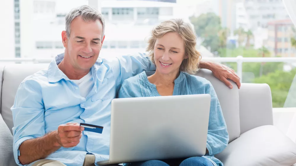 Smiling couple sitting on their couch using the laptop to buy online at home in the sitting room