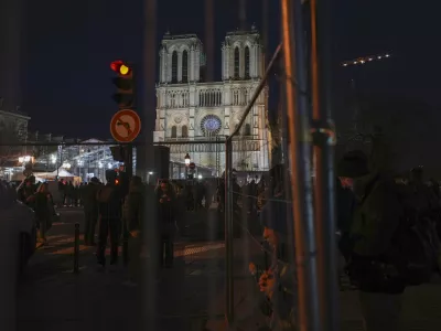 People walk past fences placed in front of Notre Dame cathedral in Paris, Friday, Dec. 6, 2024. (AP Photo/Alessandra Tarantino)