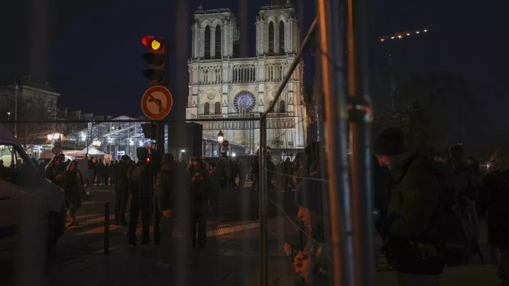 People walk past fences placed in front of Notre Dame cathedral in Paris, Friday, Dec. 6, 2024. (AP Photo/Alessandra Tarantino)