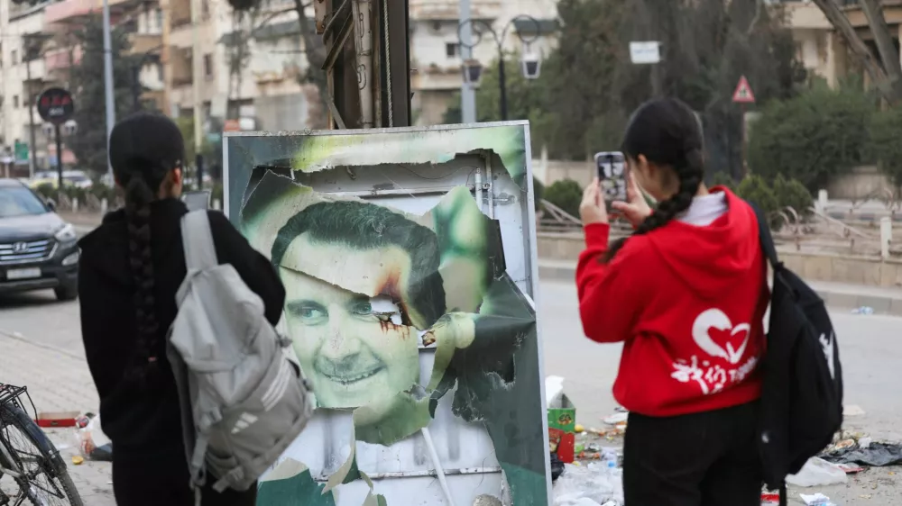 Women use their mobile phones near a damaged picture of Syrian President Bashar al-Assad as people celebrate, after Syrian rebels announced that they have ousted President Bashar al-Assad, in Qamishli, Syria December 8, 2024. REUTERS/Orhan Qereman