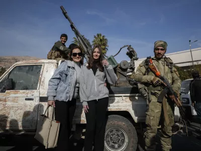 Syrian women pose for a photograph as they stand next to opposition fighters in Damascus, Syria, Tuesday, Dec. 10, 2024. (AP Photo/Omar Sanadiki)