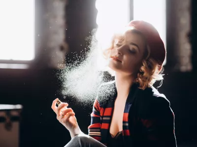 A beautiful blonde girl in a red beret holds a small bottle in her hands spraying perfume on herself enjoys armature. Backlight, soft focus.