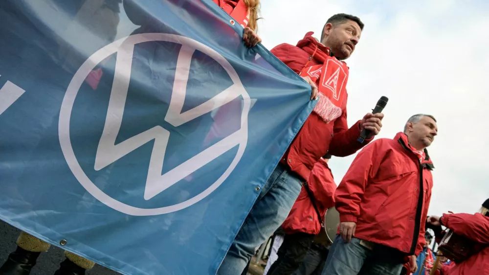 FILE PHOTO: A man wearing an IG Metall (Industrial Union of Metalworkers) scarf holds a banner with the Volkswagen logo, as workers gather to strike against planned cuts to wages and possible factory closures, in Hanover, Germany, December 2, 2024. Picture taken with long exposure. REUTERS/Fabian Bimmer/File Photo