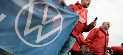 FILE PHOTO: A man wearing an IG Metall (Industrial Union of Metalworkers) scarf holds a banner with the Volkswagen logo, as workers gather to strike against planned cuts to wages and possible factory closures, in Hanover, Germany, December 2, 2024. Picture taken with long exposure. REUTERS/Fabian Bimmer/File Photo