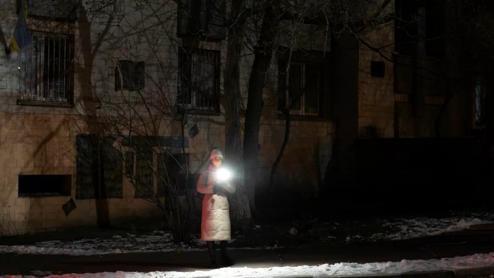 A woman holds a torch as she stands in a dark street during partial power cuts following a Russian attack on Ukrainian energy facilities, amid Russia's attack on Ukraine, in central Kyiv, Ukraine, December 13, 2024. REUTERS/Thomas Peter