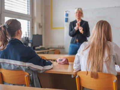 Rear view of two female students during a lecture in the classroom, looking at female teacher teaching and writing on a blackboard / Foto: 24k-production