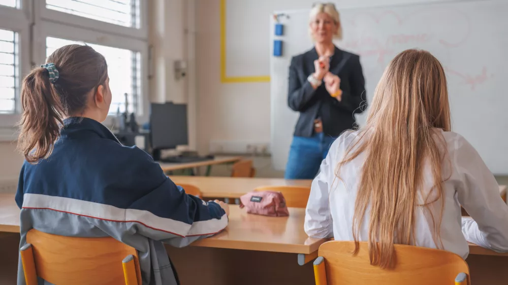 Rear view of two female students during a lecture in the classroom, looking at female teacher teaching and writing on a blackboard / Foto: 24k-production