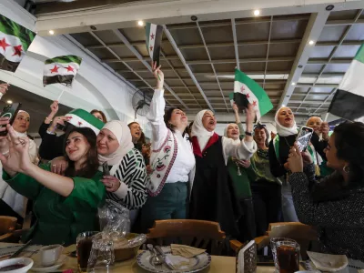 Syrian women wave "revolutionary" Syrian flags as they celebrate in a restaurant in Damascus, Syria, Tuesday, Dec. 17, 2024. (AP Photo/Omar Sanadiki)