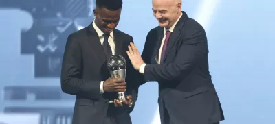 FIFA president Gianni Infantino, right, hugs Vinicius Junior of Real Madrid as he is awarded as the Best Men's FIFA Player during the FIFA Football Awards 2024 in Doha, Qatar, Tuesday, Dec. 17, 2024. (AP Photo/Hussein Sayed)