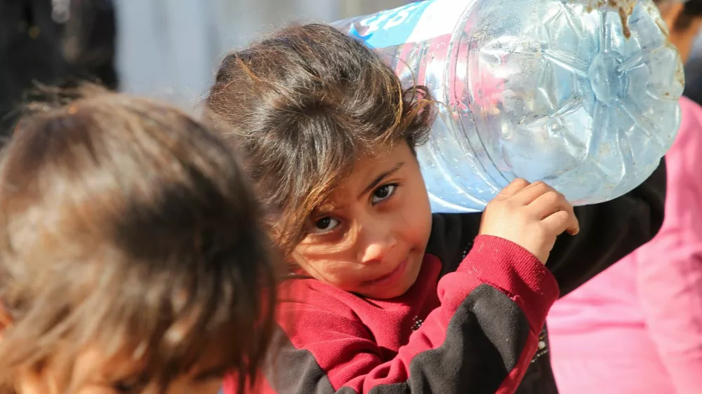 A Palestinian child carries a water container, as Palestinians wait to collect water following a Human Rights Watch report that says Israel's deprivation of water in Gaza is an act of genocide, amid the ongoing conflict between Israel and Hamas, in Khan Younis in the southern Gaza Strip December 19, 2024. REUTERS/Hatem Khaled    TPX IMAGES OF THE DAY