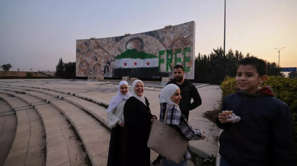 People stand near a graffiti of the Syrian rebels flag painted on a mosaic of former Syrian president Hafez al-Assad after the ousting of President Bashar al-Assad, in Damascus Syria January 2, 2025. REUTERS/Zohra Bensemra   TPX IMAGES OF THE DAY