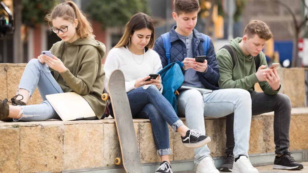 Four teenagers chatting on their smartphone on walking