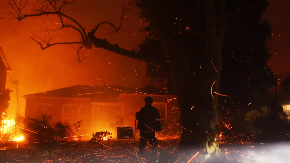 FILE - A person tries to hose down embers from the Palisades Fire in the Pacific Palisades neighborhood of Los Angeles, Jan. 7, 2025. (AP Photo/Etienne Laurent, File)