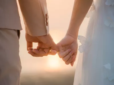 The bride and groom use the little finger together. lovely couple hold hand with sunset background