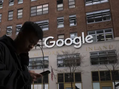 FILE - In this Dec. 17, 2018, file photo a man using a mobile phone walks past Google offices in New York. Google says it plans to launch a video-game streaming platform called Stadia, positioning itself to take on the traditional video-game business. (AP Photo/Mark Lennihan, File)