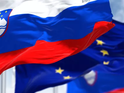 Detail of the national flag of Slovenia waving in the wind with blurred european union flag in the background on a clear day. Democracy and politics. European country. Selective focus.