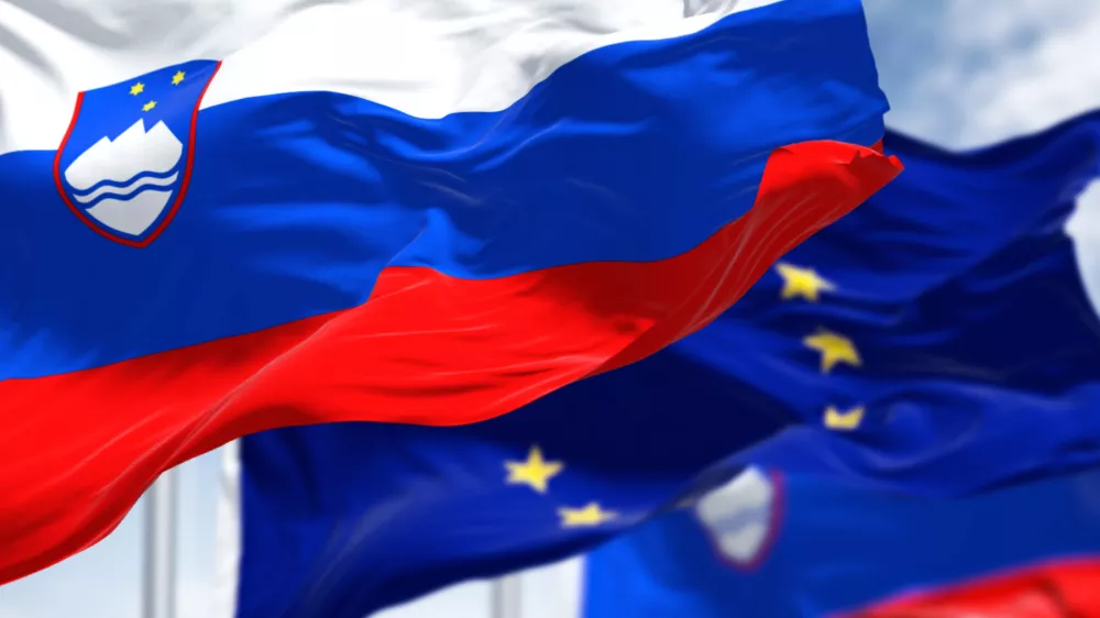 Detail of the national flag of Slovenia waving in the wind with blurred european union flag in the background on a clear day. Democracy and politics. European country. Selective focus.