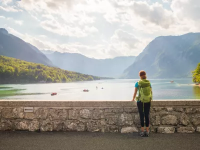 Young woman wearing green backpack is standing on the bridge near Bohinj lake looking at the view in Bohinj, Slovenia